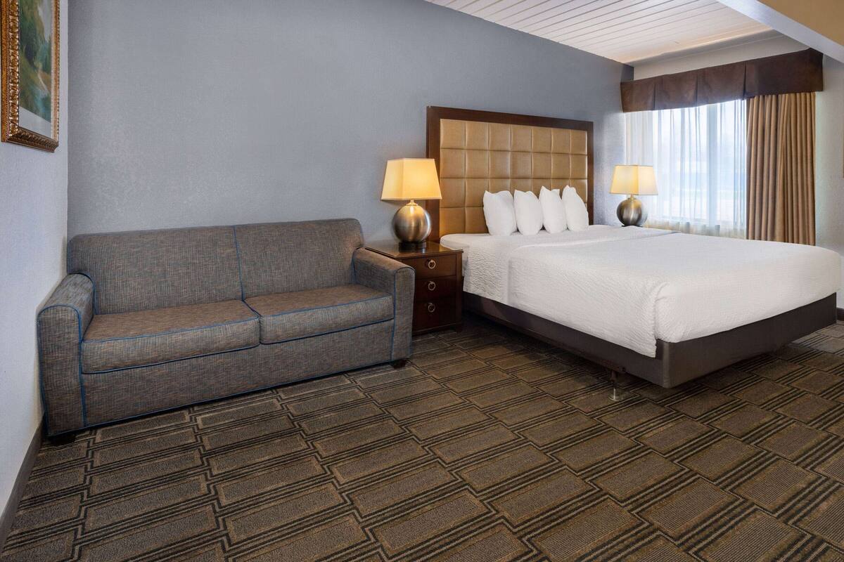 A hotel room with a bed, a sofa, two bedside tables with lamps, and a patterned carpet.