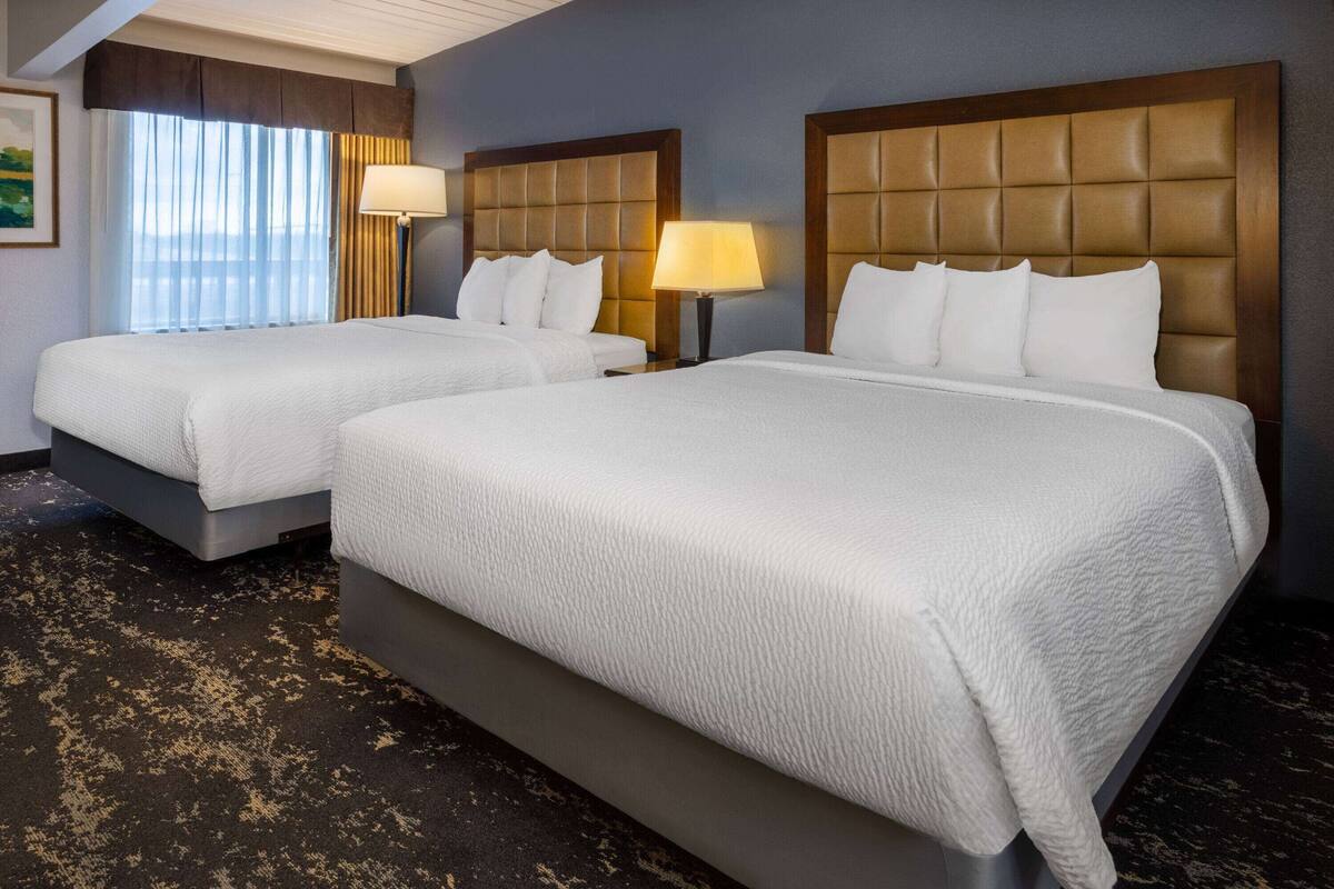 A hotel room with two beds, each with a headboard and a bedside lamp.