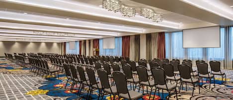 Un salón de conferencias con filas de sillas, una alfombra grande con estampado floral y una pantalla para proyector.