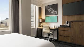 Ein Hotelzimmer mit einem großen Bett, einem Schreibtisch mit Stuhl, einem Fernseher und einer Kaffeemaschine.