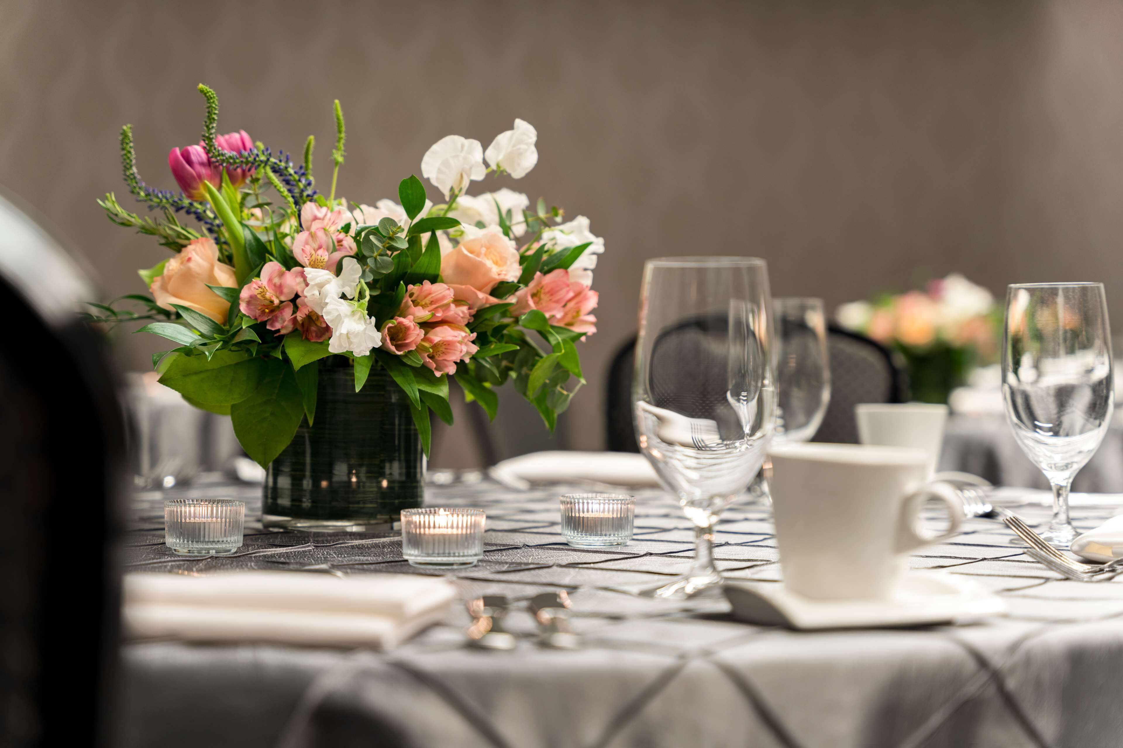 A dining table set with a vase of flowers, candles, and glassware.