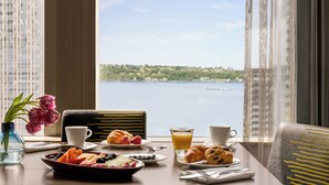 Une table de petit-déjeuner avec des croissants, des fruits et du jus, donnant sur un lac avec une vue sur la ville en arrière-plan.