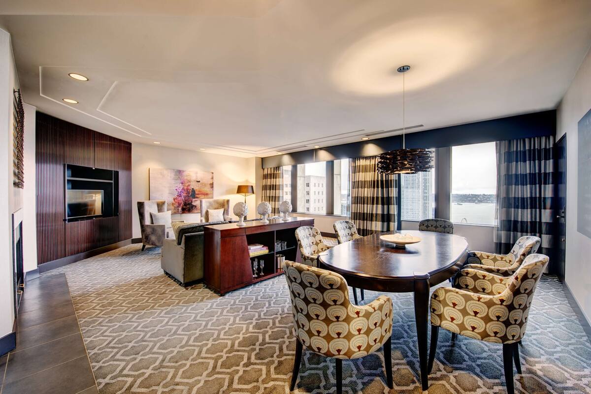 A modern dining area with a round table, patterned chairs, a wooden cabinet, and a large window with curtains.