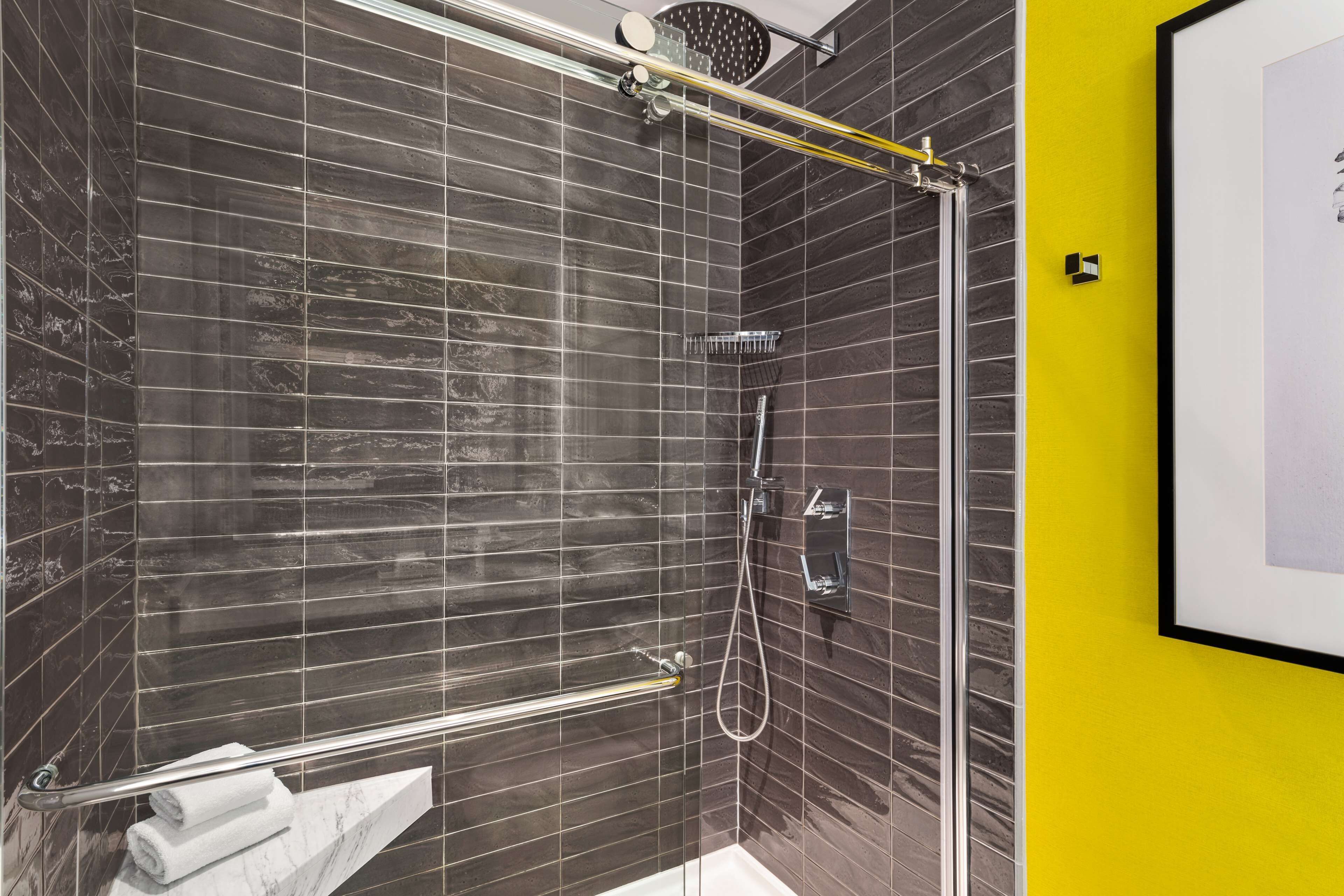 Une salle de bain moderne avec des murs recouverts de carreaux foncés, une douche en verre et un mur d’accent jaune.