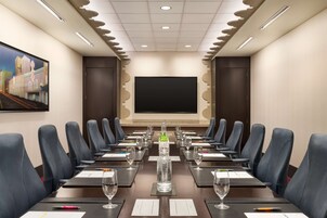 Un salón de conferencias con una mesa larga, sillas de cuero negro y una pantalla grande al frente.