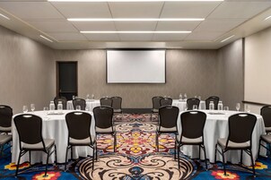 A conference room with a large screen, round tables, and chairs.