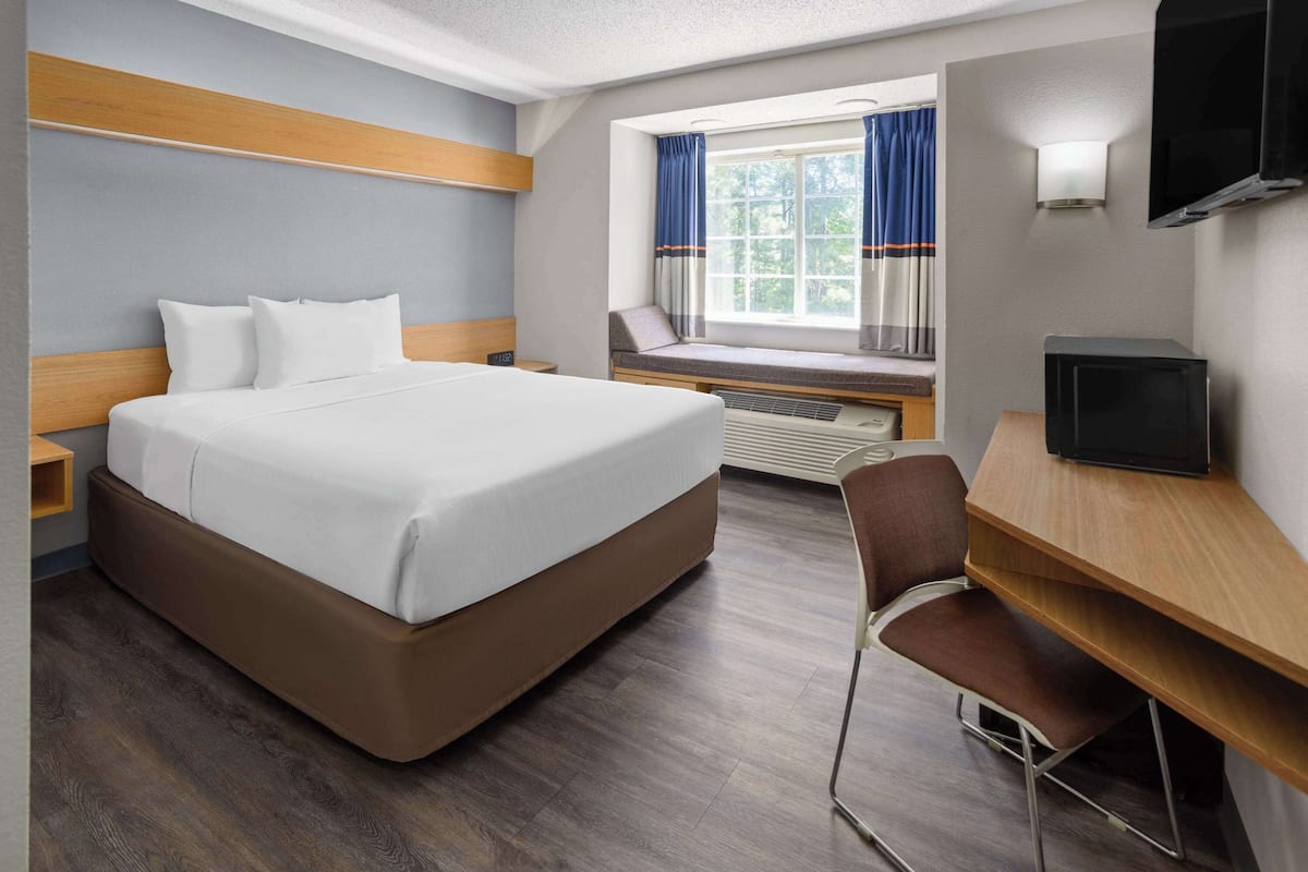 Une chambre d’hôtel avec un grand lit, un bureau avec une chaise, une télévision et une fenêtre avec des rideaux.