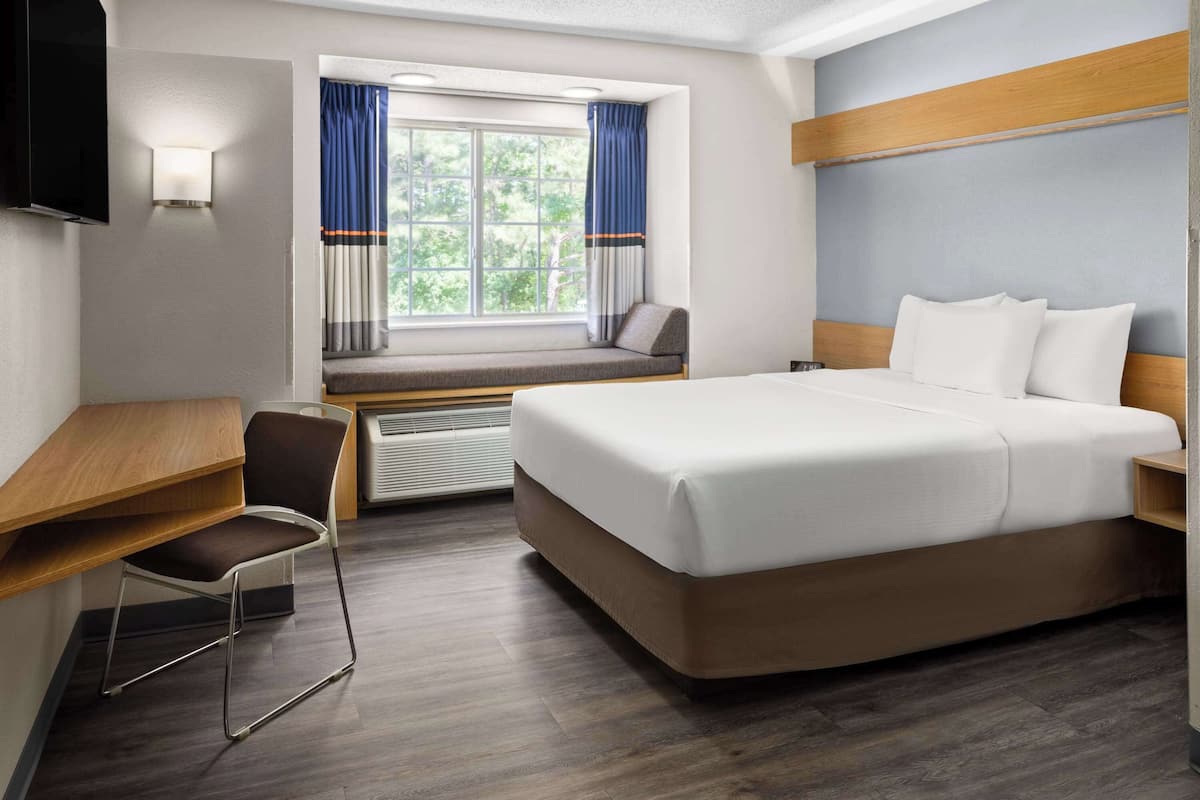 Une chambre d’hôtel avec un lit, un bureau, une chaise, une télévision et une fenêtre avec des rideaux.