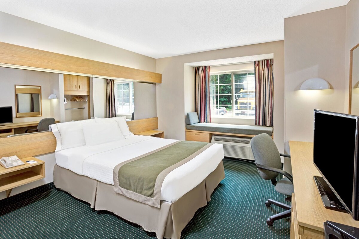 A hotel room with a bed, desk, chair, TV, and window with curtains.