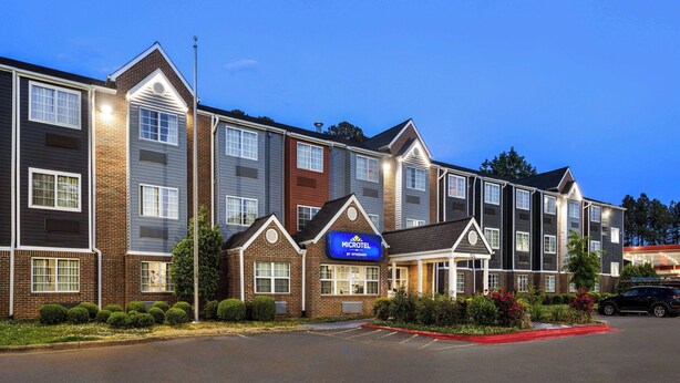 A Microtel by Wyndham hotel with a brick facade, multiple windows, and a parking lot. - Microtel Inn by Wyndham Raleigh Durham Airport (Morrisville)