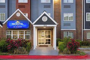 A Microtel Inn by Wyndham building with a brick facade, a blue sign, and a number 104 entrance. - Microtel Inn by Wyndham Raleigh Durham Airport (Morrisville)