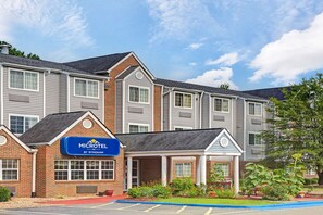 A Microtel Inn by Wyndham with a brick facade, multiple windows, and a landscaped garden area. - Microtel Inn by Wyndham Raleigh Durham Airport (Morrisville)