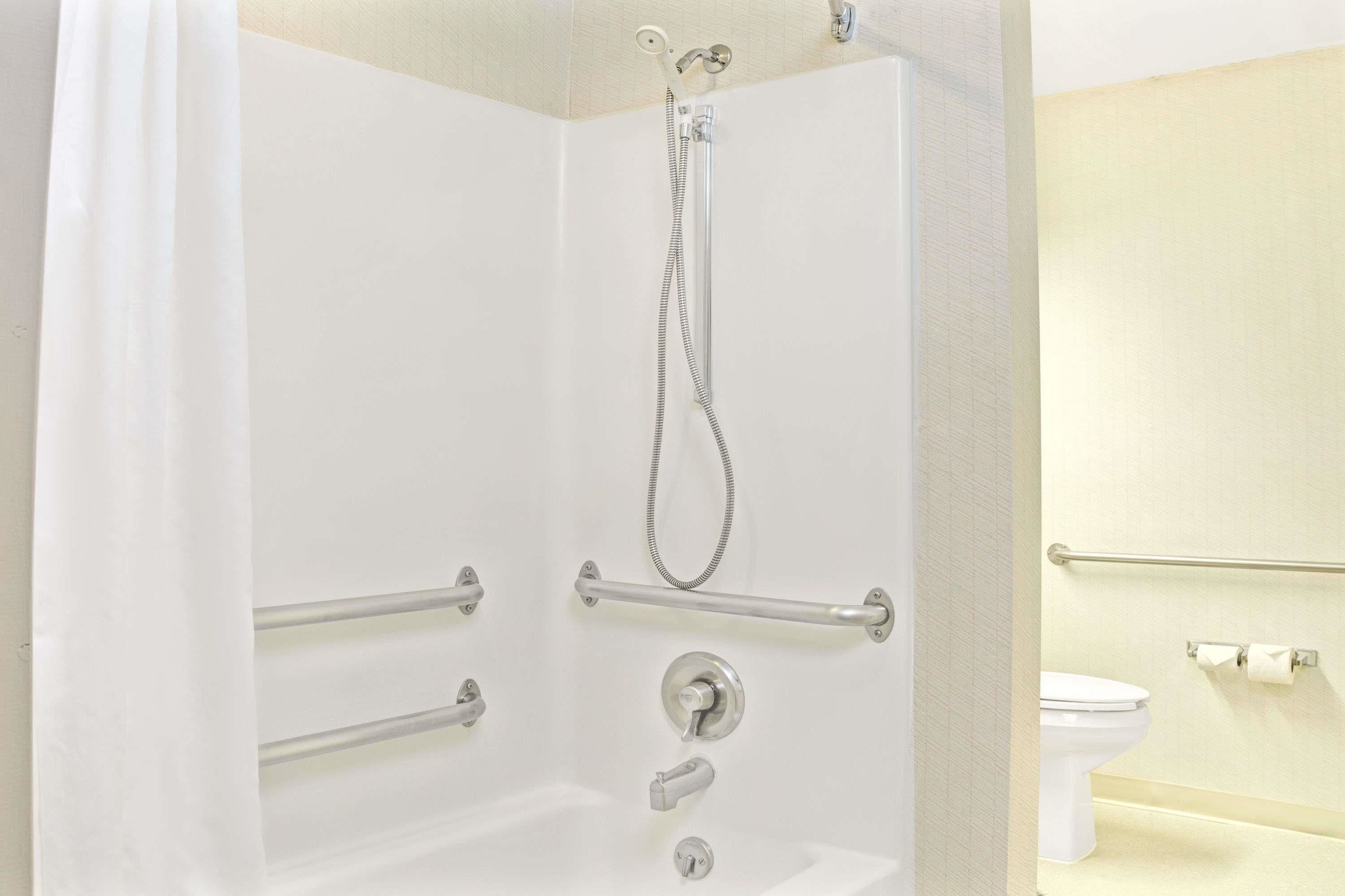 A shower with grab bars, a handheld showerhead, and a toilet with a grab bar.