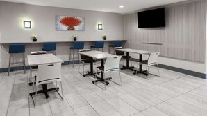 A conference room with six tables and chairs, a flat-screen TV mounted on the wall, and decorative wall art. - Microtel Inn by Wyndham Raleigh Durham Airport (Morrisville)