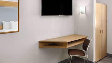 A modern hotel room with a built-in desk, a chair, a wardrobe, and a flat-screen TV mounted on the wall.
