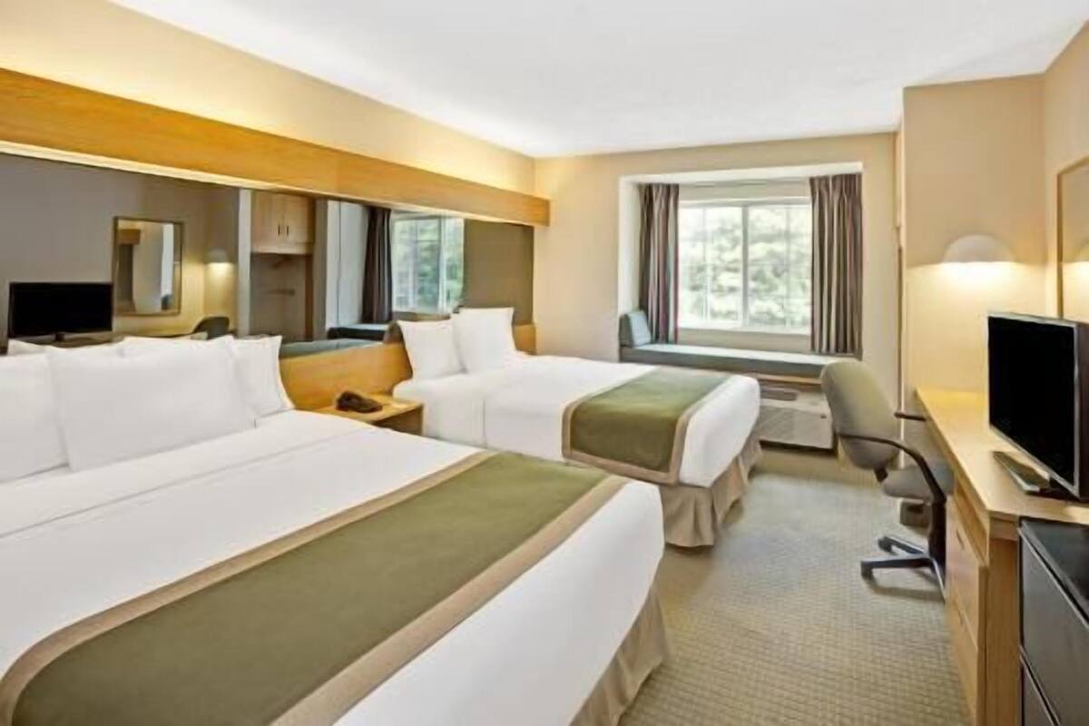 Une chambre d’hôtel avec deux lits, un bureau, une chaise, une télévision et une fenêtre.