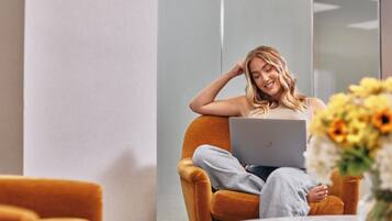 A person sitting on a chair with a laptop, in a room with a glass partition and a table with flowers.