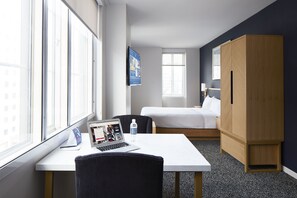 A hotel room with a bed, a desk with a laptop, a chair, and a wardrobe.