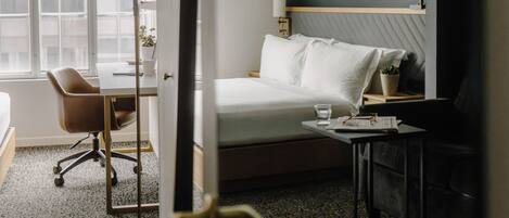 A hotel room with a bed, bedside table, lamp, chair, and a view of the outside through a window.