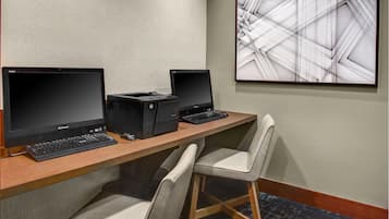 A workspace with two Lenovo monitors, a printer, and a keyboard on a wooden desk. There are two chairs and a large abstract painting on the wall.
