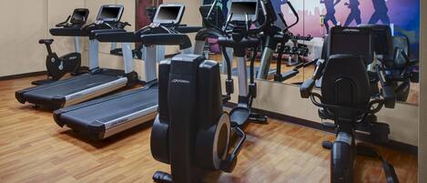 A gym with treadmills, elliptical machines, and a mirrored wall with a cityscape mural.