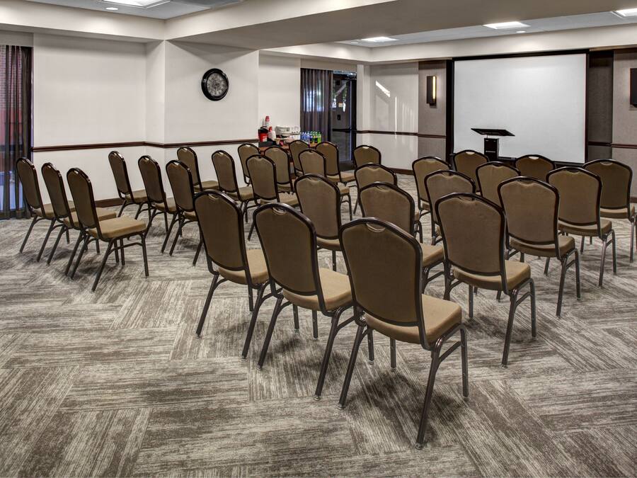 A conference room with rows of chairs, a projector screen, and a clock on the wall.