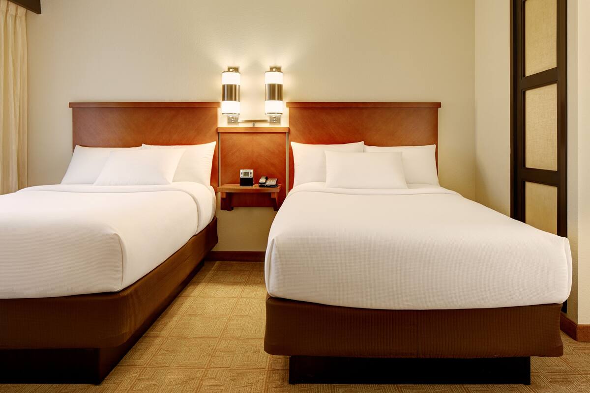 Two single beds with wooden headboards, a nightstand with a phone, and a wall-mounted light fixture.