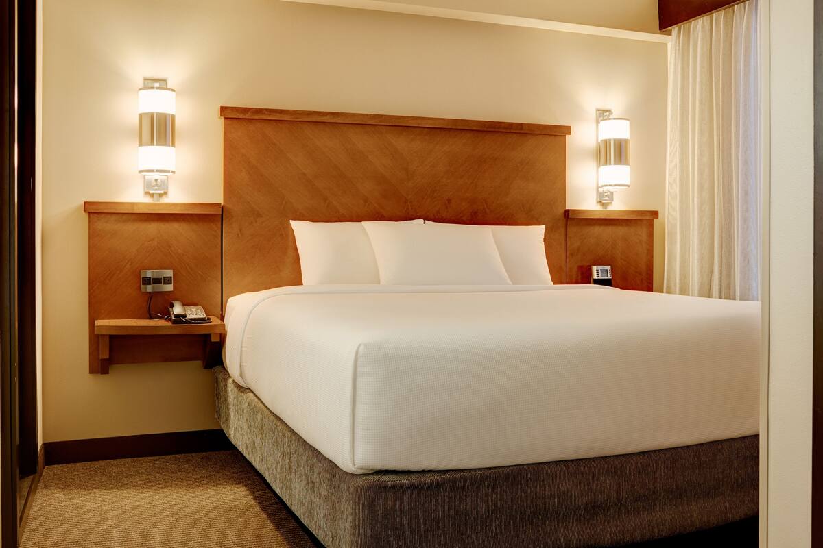 A hotel room with a large bed, wooden headboard, bedside lamps, and a telephone on a nightstand.
