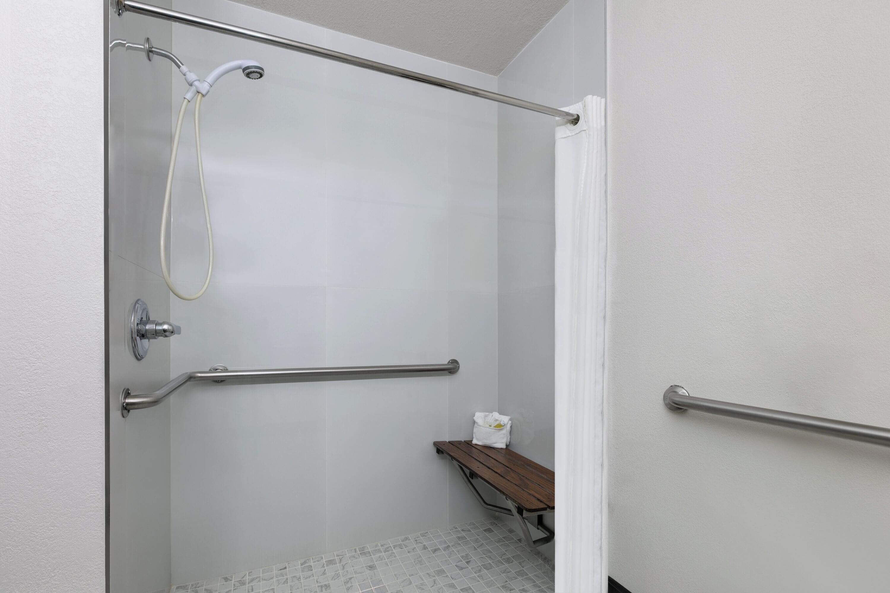 A shower area with a glass door, a bench, and a handrail.