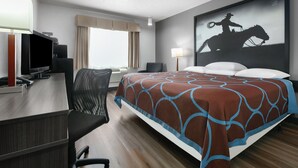 Habitación de hotel con cama, escritorio con computadora, una silla, ventana con cortinas y lámpara de pared.