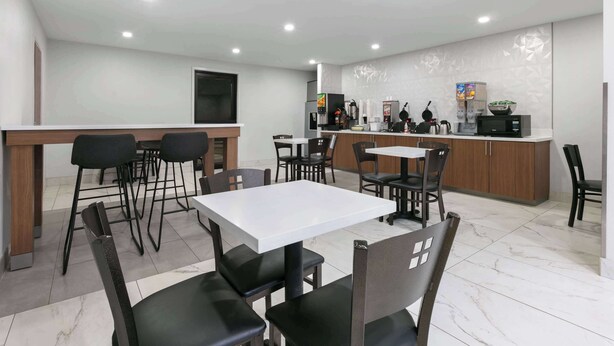 Una cocina moderna con encimeras blancas, sillas negras y una mesa blanca.