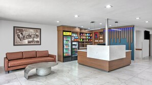 Un área de recepción moderna con un mostrador de madera, un sofá de cuero marrón, una mesa de centro de mármol y un refrigerador lleno de bebidas.