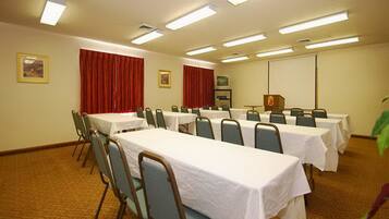 Un salón de conferencias con varias mesas y sillas, equipado con luces en el techo y una pantalla de proyector.