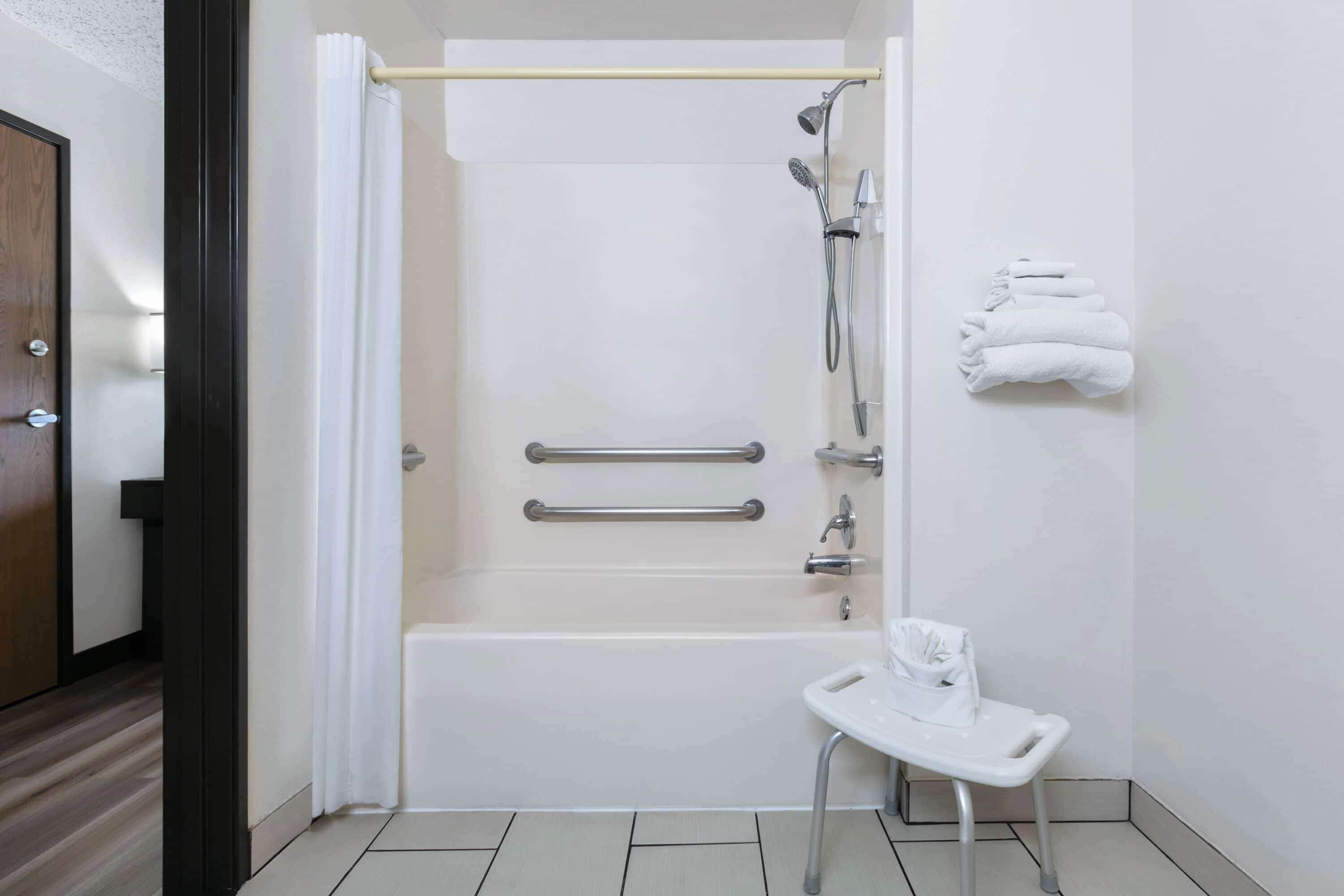 A bathroom with a bathtub, a shower, a handrail, a towel rack, and a small white sink.