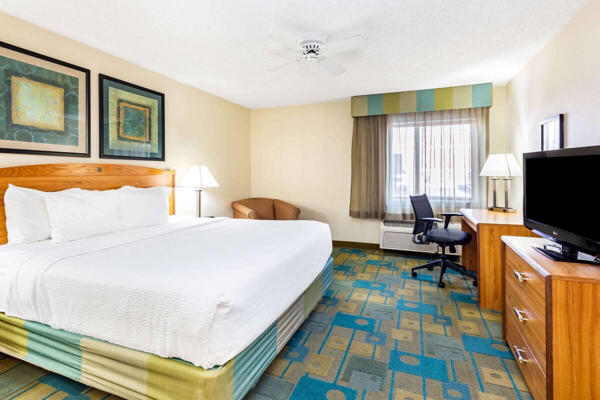 Een hotelkamer met een groot bed, een bureau met een televisie, een stoel en twee kunstwerken in lijsten aan de muur.