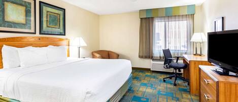 A hotel room with a large bed, a desk with a television, a chair, and two framed artworks on the wall.