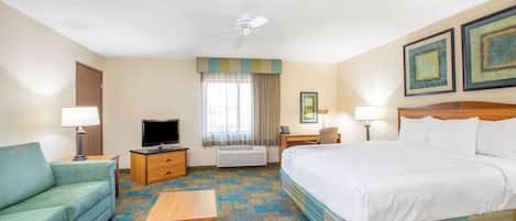 A hotel room with a bed, a sofa, a TV, a desk, and a ceiling fan.