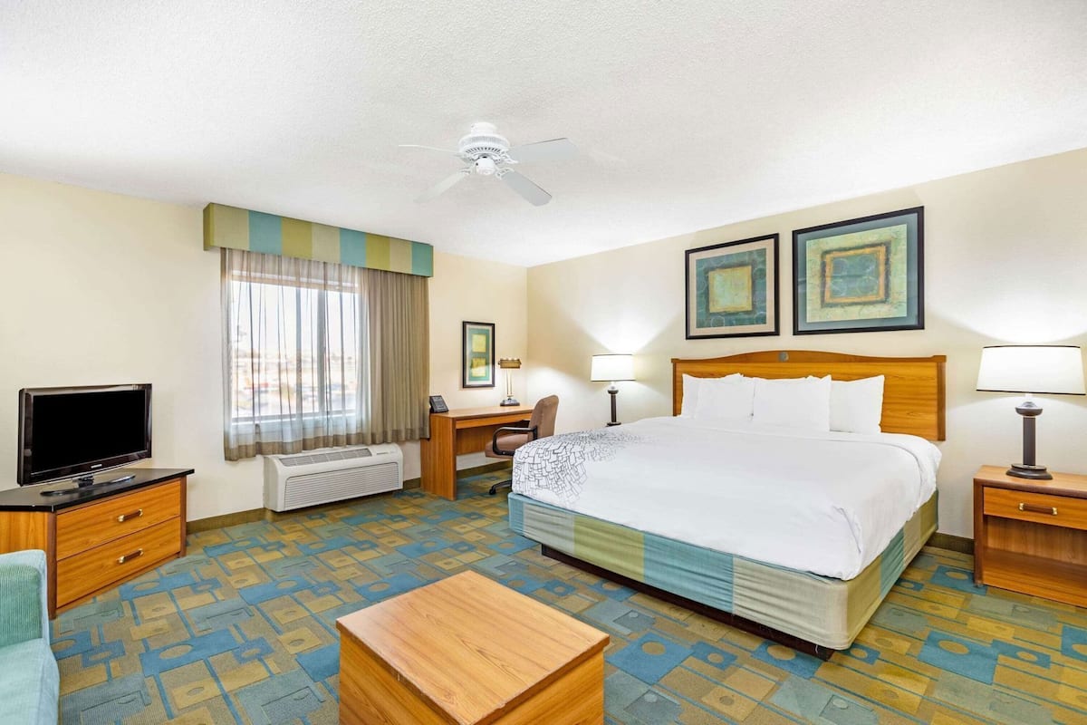 Habitación de hotel con cama, escritorio, silla, televisor y ventilador de techo.