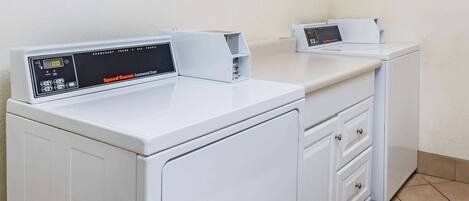 A laundry room with two white commercial dryers, a control panel, and a tiled floor.