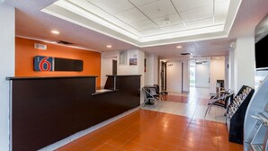 Zona de recepción de hotel con un mostrador oscuro, un letrero que indica la habitación número 6, una máquina expendedora y un mueble con revistas.