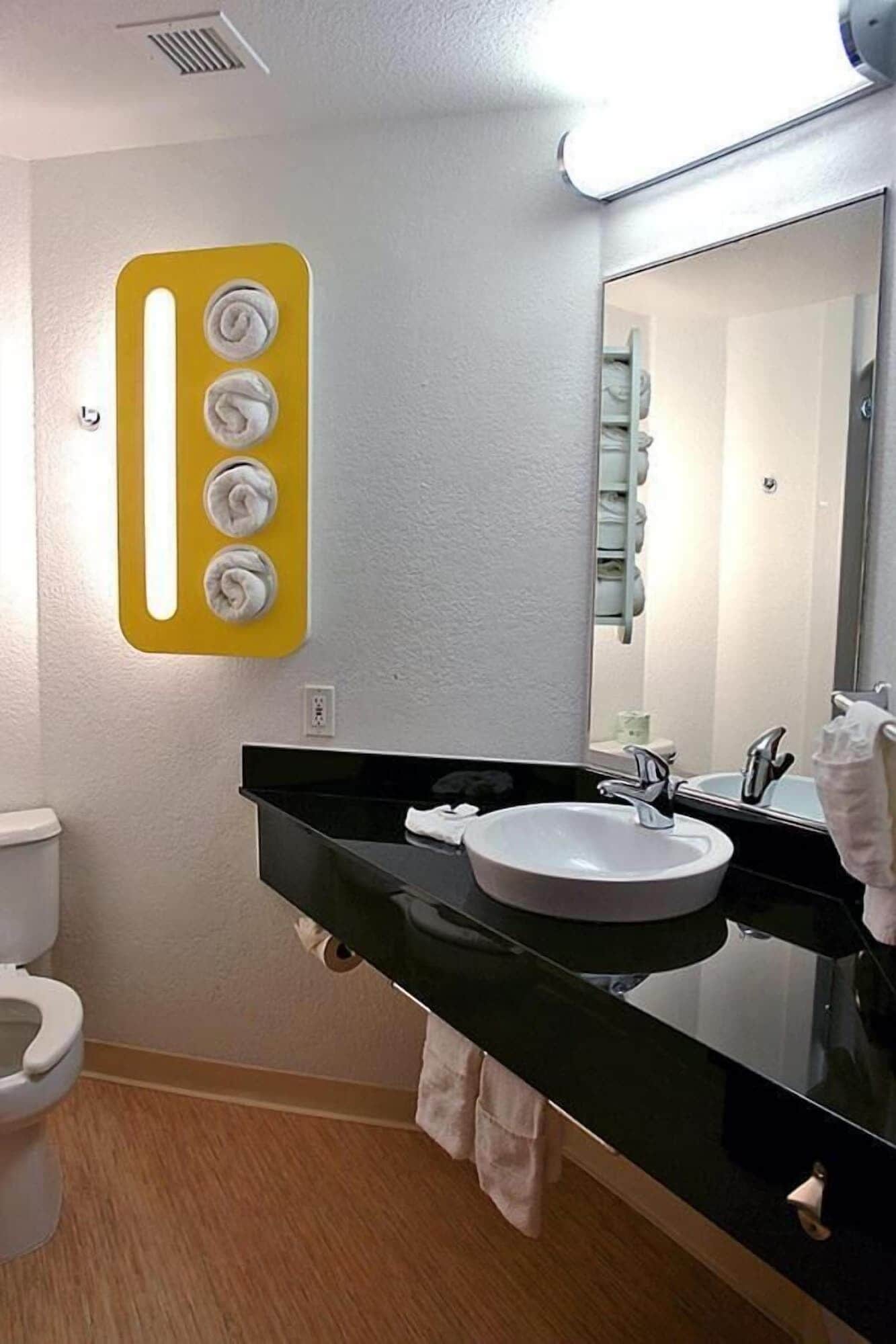 A bathroom with a white toilet, a black sink with a mirror above it, and a yellow light fixture with four bulbs.