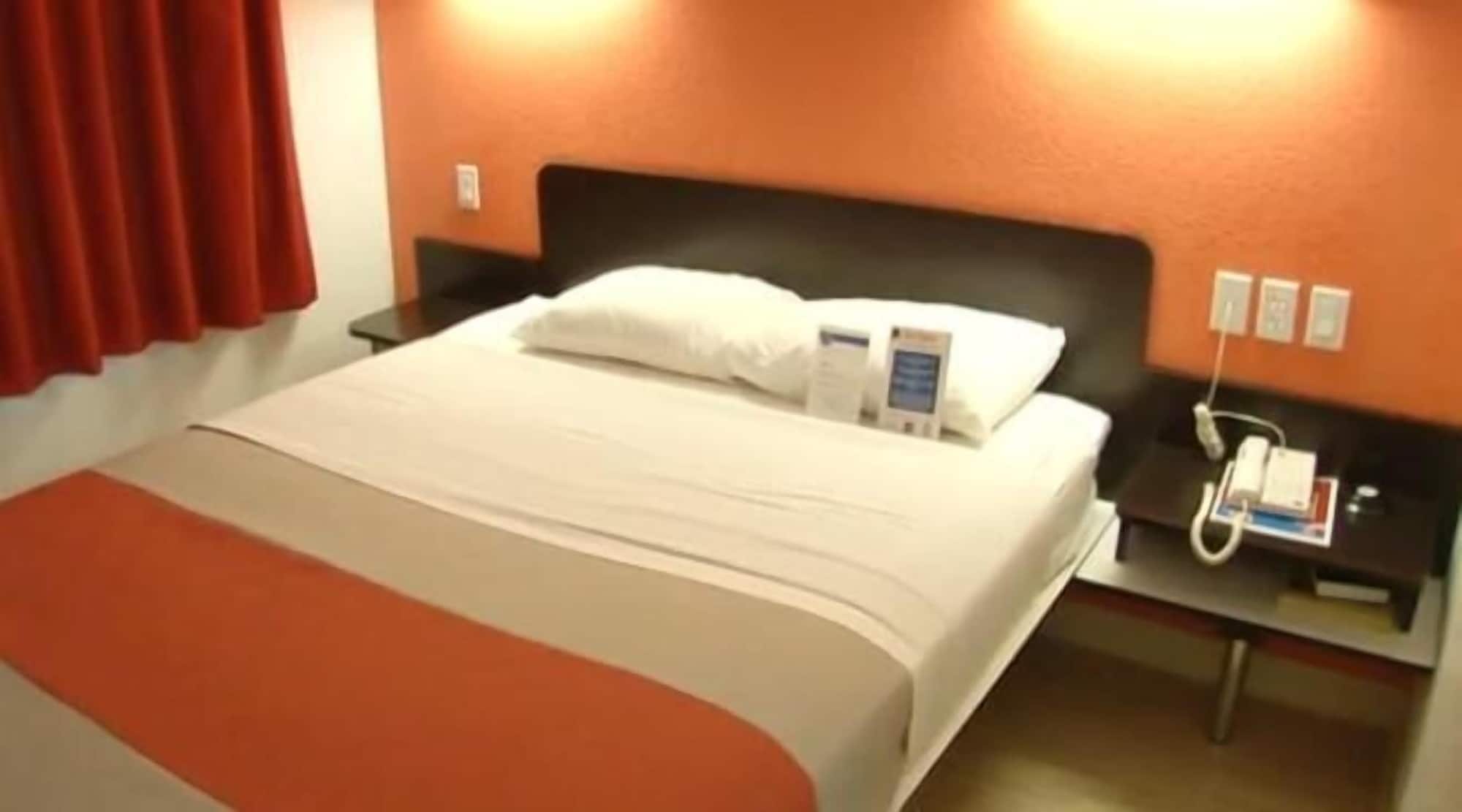 A hotel room with a bed, a bedside table with a phone, and a wall socket.