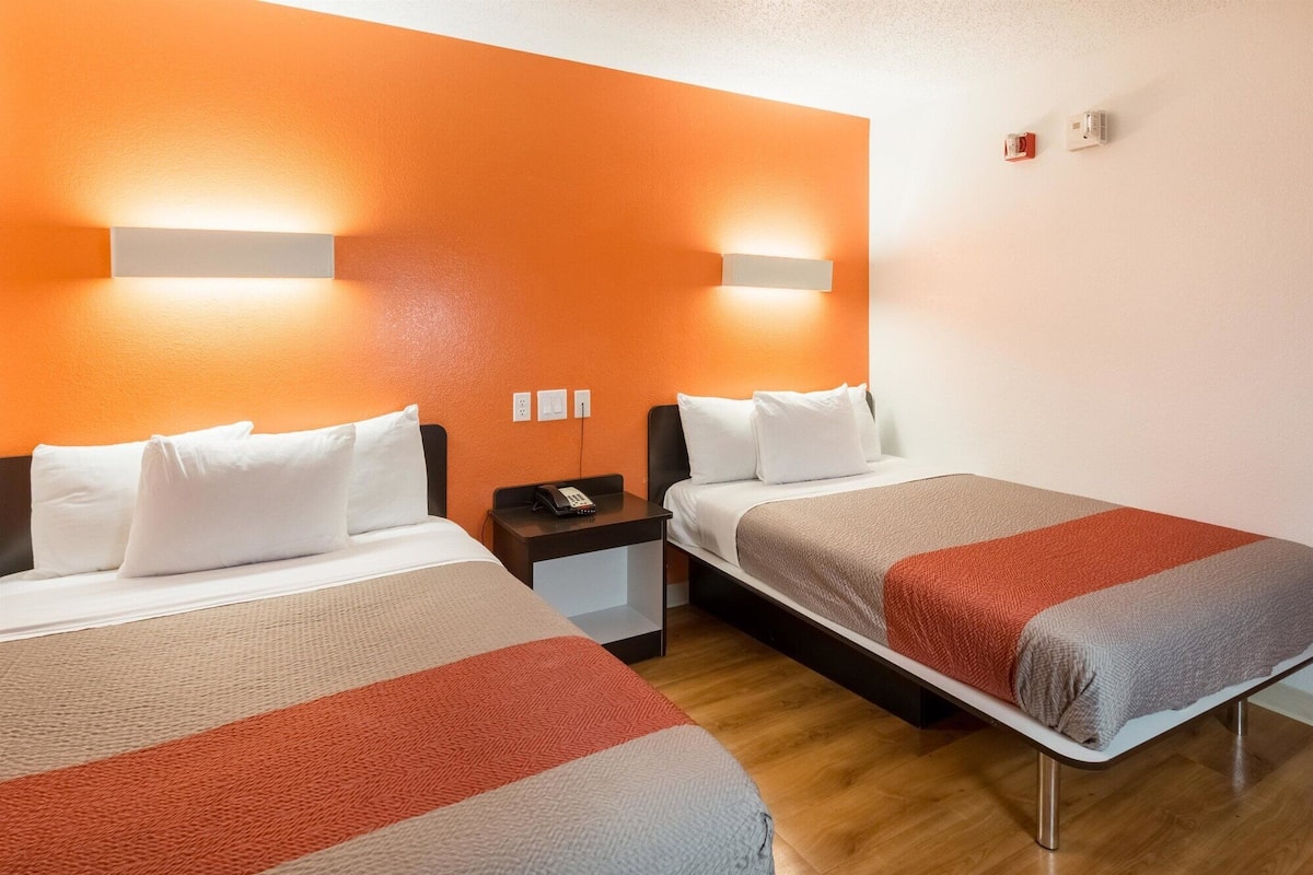 Une chambre d’hôtel avec deux lits, une table de chevet et un téléphone fixé au mur.