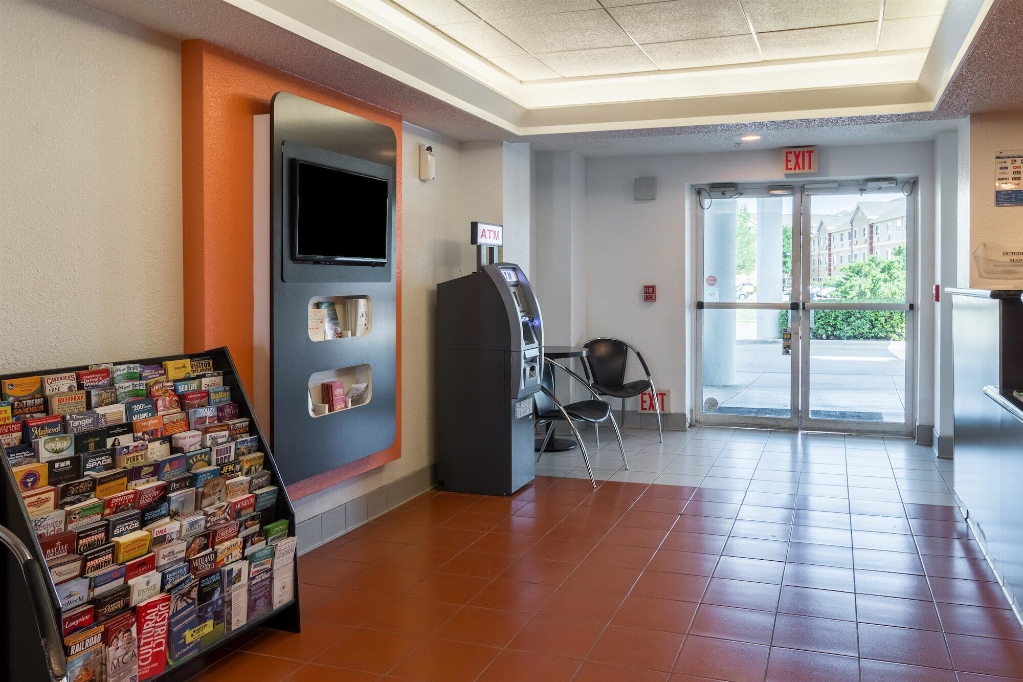 A lobby with an ATM, a fire alarm, and a chair near the exit doors.
