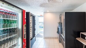 Zona con máquinas expendedoras de Coca-Cola y otras bebidas, un cubo de basura y un microondas.