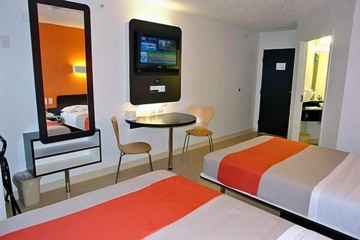 Une chambre d’hôtel avec deux lits, une télévision, une petite table et deux chaises.