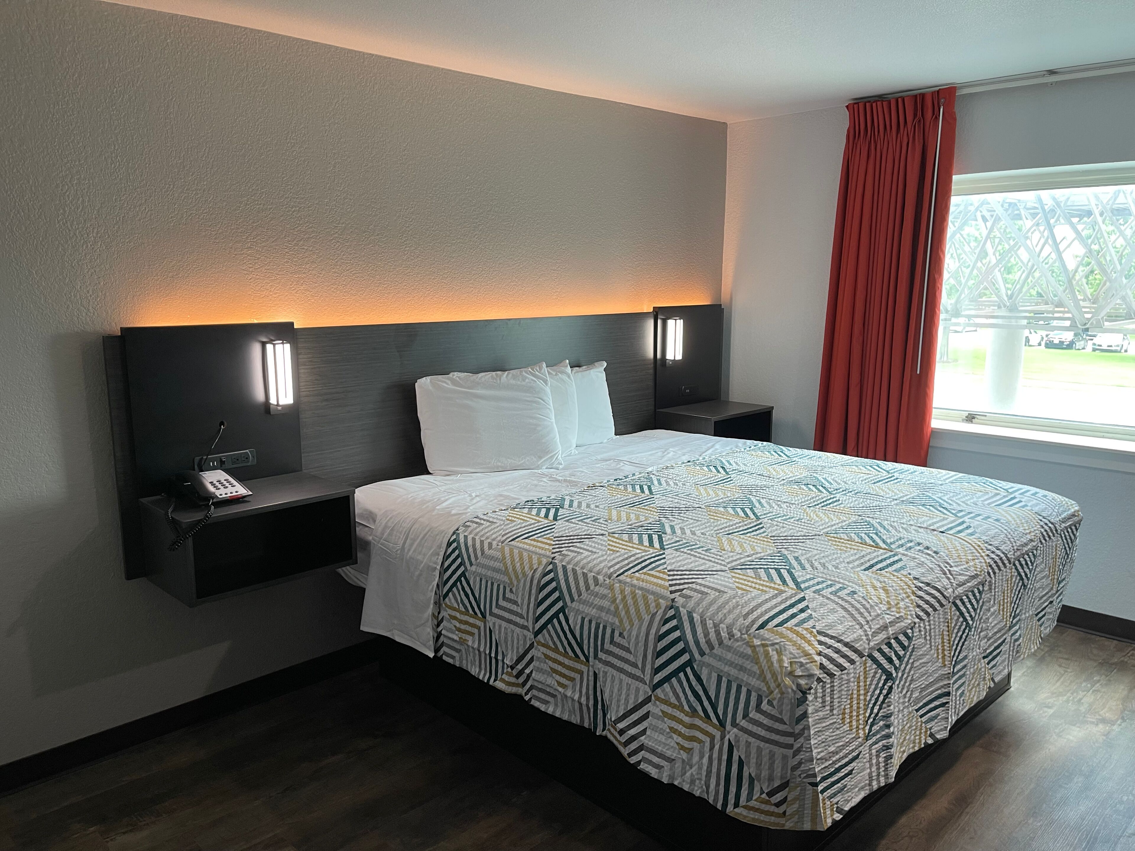 Habitación de hotel con cama, dos mesitas de noche, teléfono y ventana con cortinas.