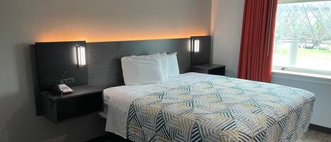 A hotel room with a bed, two bedside tables, a telephone, and a window with curtains.