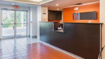 A hotel reception area with a modern design, including a reception desk, a digital screen, and a sign indicating the hotel name 'motel 6'.