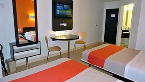 Habitación de hotel con dos camas, un televisor montado en la pared, una mesita redonda y una silla.